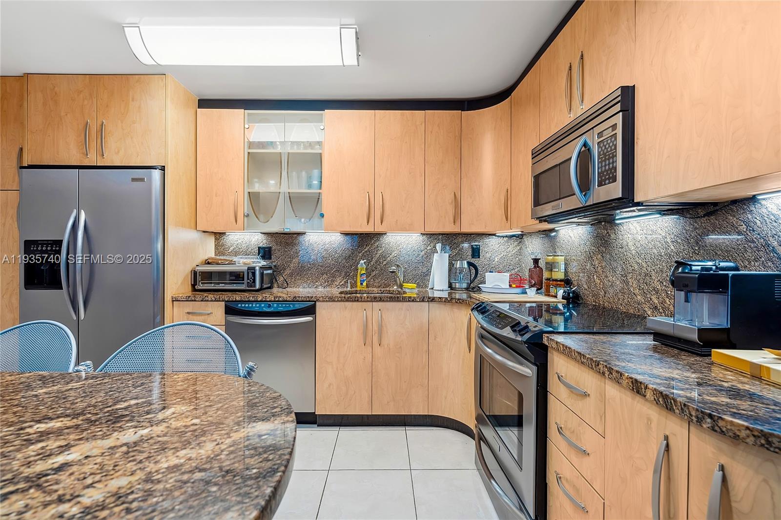 A kitchen features light wood cabinets, granite countertops, stainless steel appliances, and tile flooring — 1400 S Ocean Dr # 802, Hollywood FL 33019, HOLLYWOOD, FL