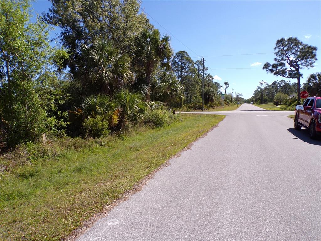 A paved road leads to a rural intersection with trees and a parked red truck — 26272 DEER ROAD, PUNTA GORDA, FL