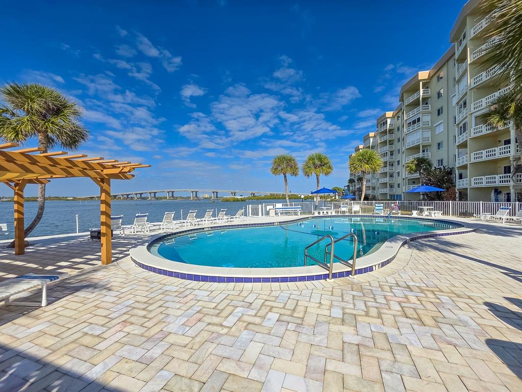 A swimming pool sits on a paved patio next to a multi-story building and water — 3606 S PENINSULA DRIVE UNIT 605, PORT ORANGE, FL
