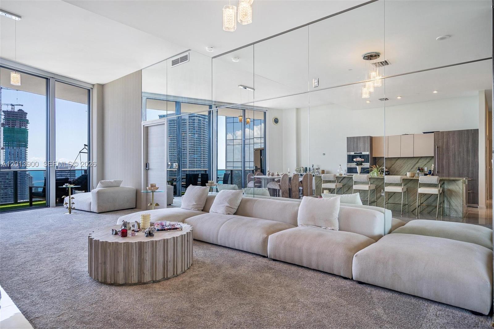 A modern living room features a large sectional sofa, mirrored wall, and floor-to-ceiling windows — 801 S Miami Ave # 5702, Miami FL 33130, MIAMI, FL
