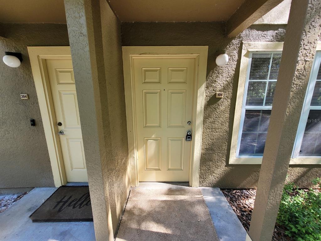 An exterior view shows two apartment entry doors numbered 104 and 204 with light-colored paint — 36106 LAKE CHASE BOULEVARD UNIT 104, ZEPHYRHILLS, FL
