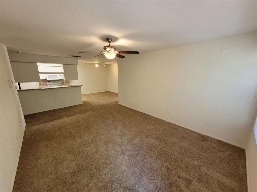 A carpeted living room opens to a kitchen with a breakfast bar and ceiling fan — 36106 LAKE CHASE BOULEVARD UNIT 104, ZEPHYRHILLS, FL