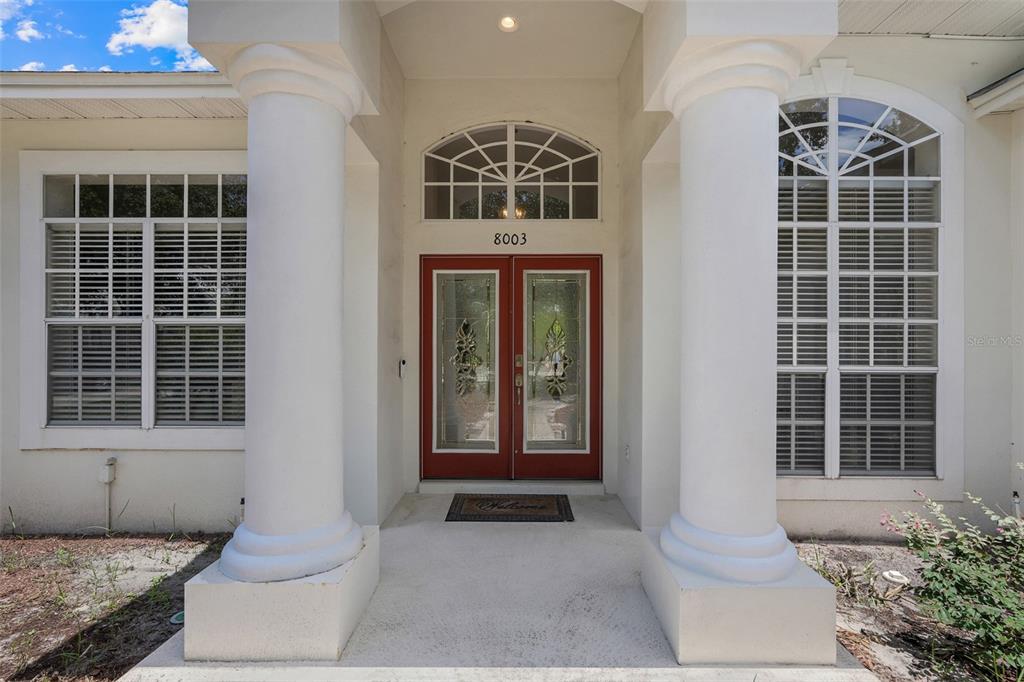 The front entrance features double red doors flanked by two large white columns — 8003 BELSHIRE DRIVE, ORLANDO, FL