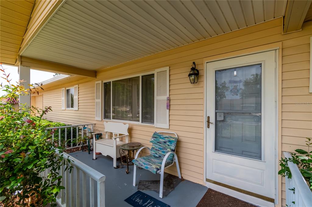 A covered front porch features light yellow siding, a white door, and outdoor seating — 8173 SW 107TH PLACE, OCALA, FL