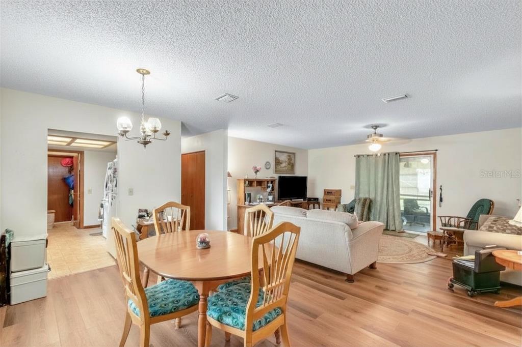 An open-concept living and dining area features wood-look flooring, a round table, and sliding doors — 8173 SW 107TH PLACE, OCALA, FL