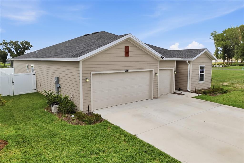 A tan-sided house features a three-car garage and a white vinyl fence on the side — 4587 SW 83RD LOOP, OCALA, FL