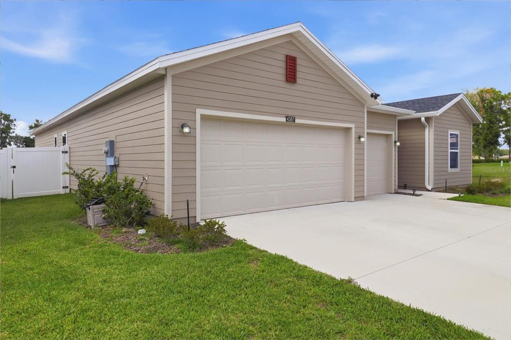 A beige house exterior features a three-car garage and a white vinyl fence — 4587 SW 83RD LOOP, OCALA, FL