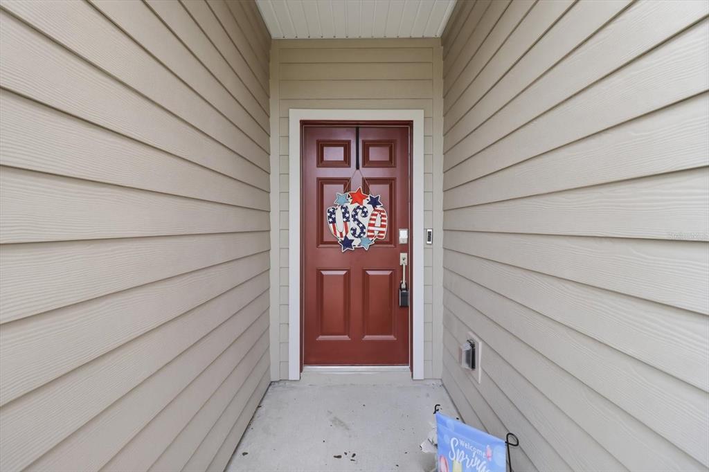 A red front door with a patriotic wreath is set between beige vinyl-sided walls — 4587 SW 83RD LOOP, OCALA, FL