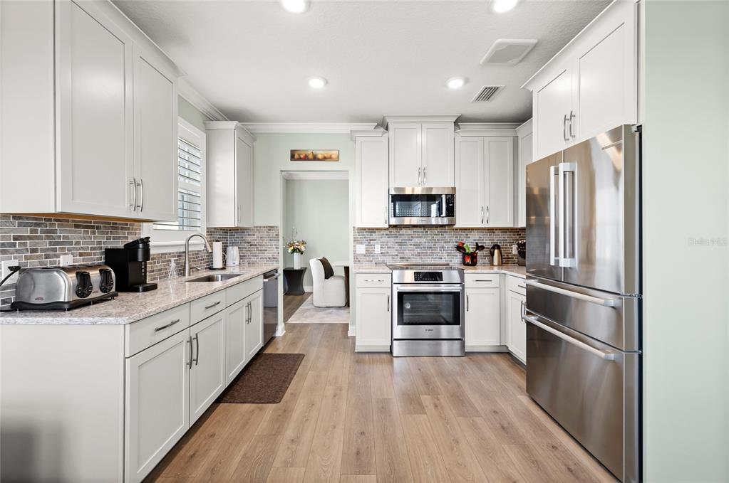 A modern kitchen features white cabinetry, stainless steel appliances, and wood-look flooring — 7505 LAUREATE BOULEVARD UNIT 2206, ORLANDO, FL