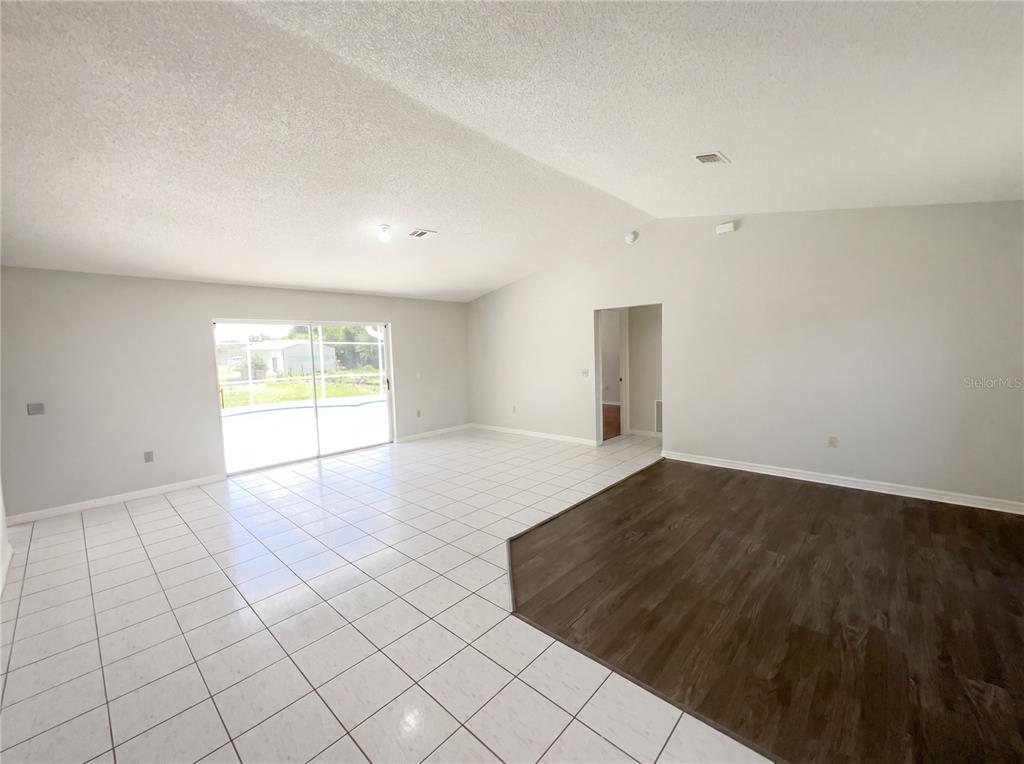 An open-concept living area features white tile flooring, dark wood-look flooring, and sliding glass doors — 1750 EVERGREEN COURT, KISSIMMEE, FL
