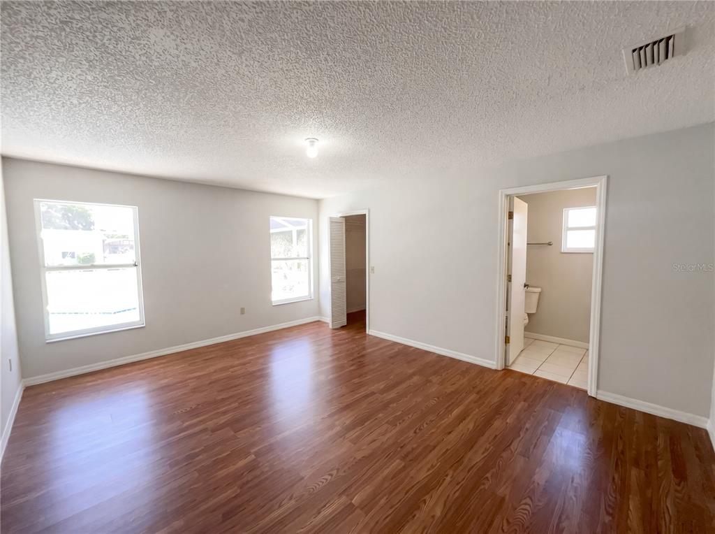 An empty bedroom features light gray walls, wood-look flooring, two windows, and an attached bathroom — 1750 EVERGREEN COURT, KISSIMMEE, FL