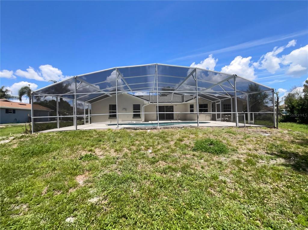 A backyard view of a house with a screened-in pool enclosure under a blue sky — 1750 EVERGREEN COURT, KISSIMMEE, FL