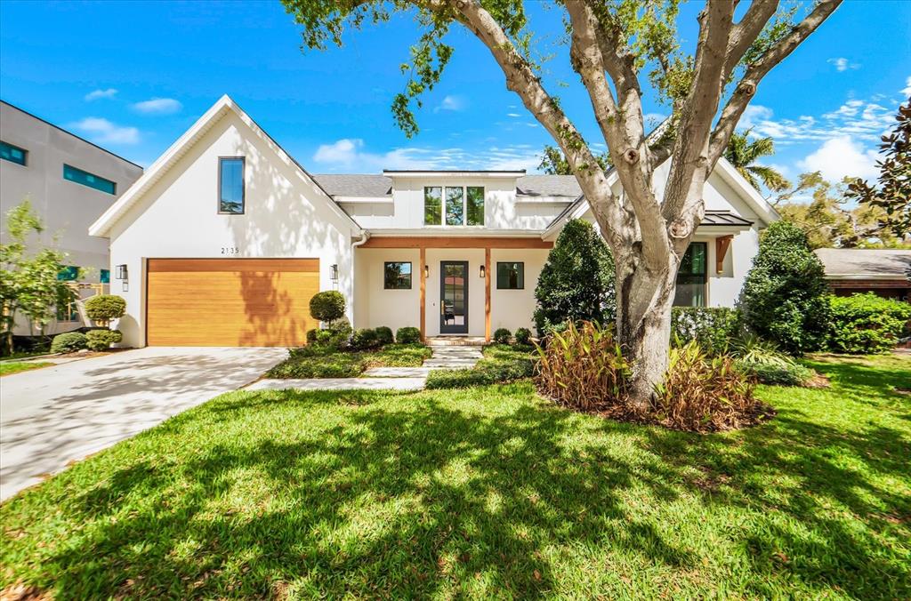 A white house with a wood garage door, a front porch, and a large tree — 2135 DATURA STREET, SARASOTA, FL