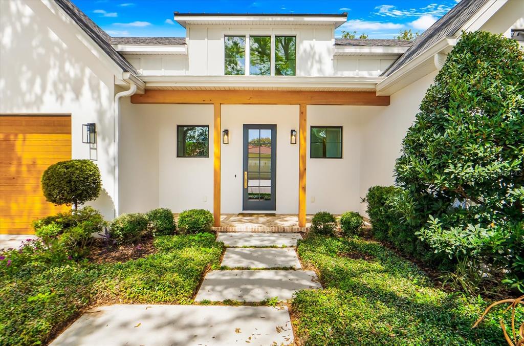 A white house exterior features a wooden beam porch, a dark door, and stone pavers — 2135 DATURA STREET, SARASOTA, FL