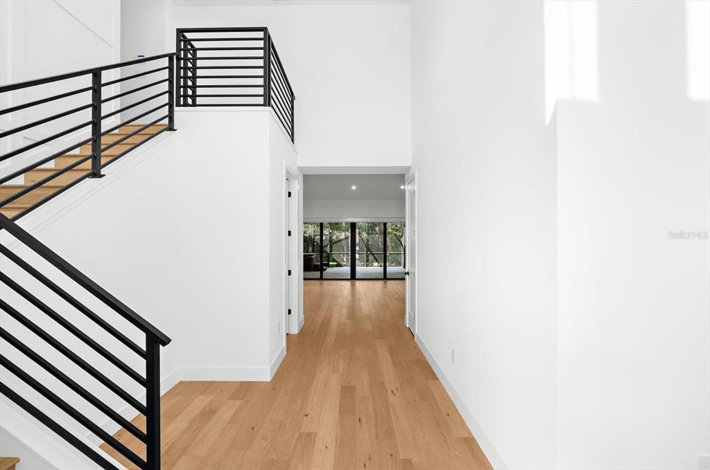 An entryway features light wood flooring, white walls, and a staircase with black metal railings — 2135 DATURA STREET, SARASOTA, FL
