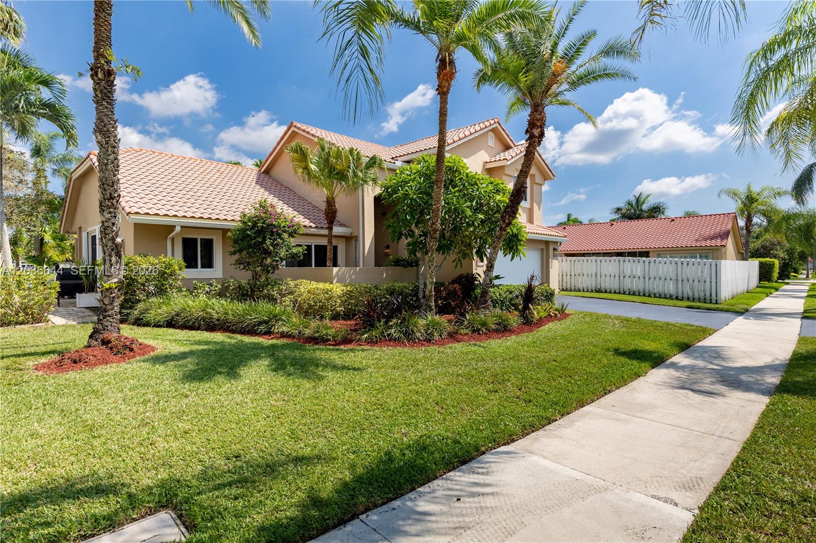 A tan two-story house with a tile roof and palm trees sits on a lawn — 1171 Laguna Springs Dr, Weston FL 33326, WESTON, FL