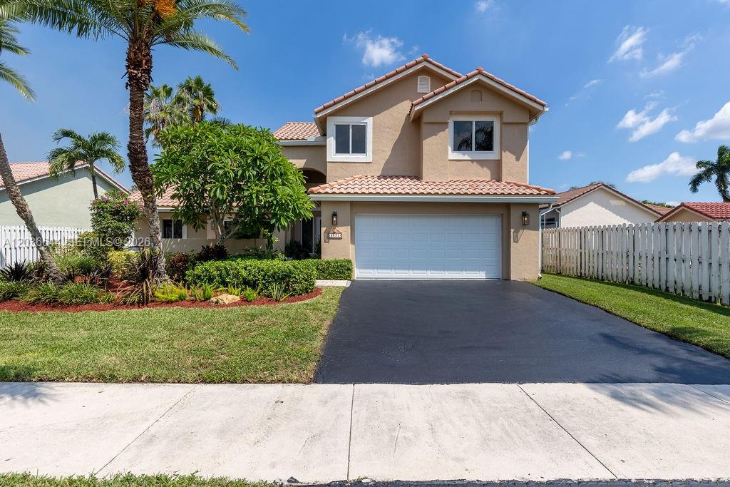 A two-story tan house with a two-car garage, tile roof, and a front lawn — 1171 Laguna Springs Dr, Weston FL 33326, WESTON, FL