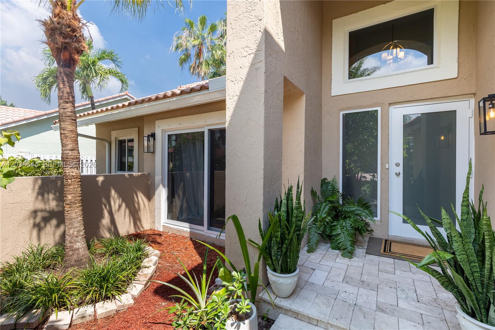 The exterior of a beige house features a palm tree, stone walkway, and front door — 1171 Laguna Springs Dr, Weston FL 33326, WESTON, FL