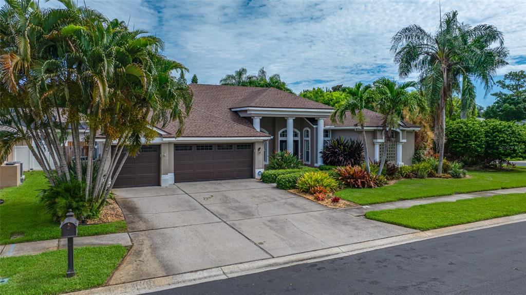A single-story house with a brown shingled roof, a three-car garage, and palm trees — 10675 PARK PLACE DRIVE, SEMINOLE, FL