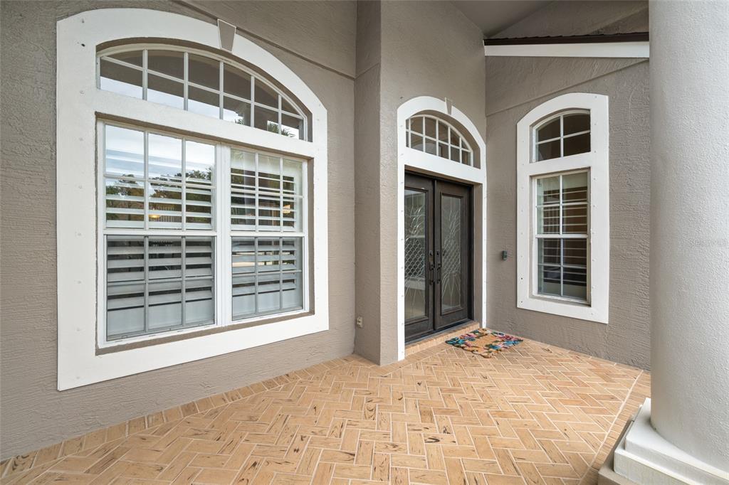 A covered entryway features a herringbone-patterned brick floor, double front doors, and arched windows — 10675 PARK PLACE DRIVE, SEMINOLE, FL