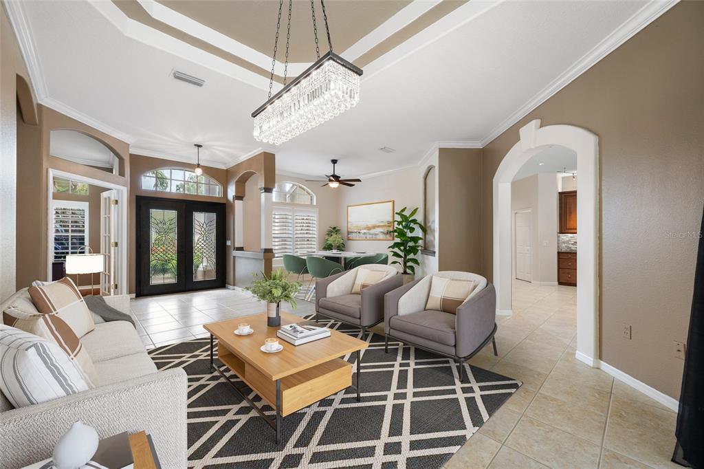 A living room with a tray ceiling, crystal chandelier, tile floors, and an arched entryway — 10675 PARK PLACE DRIVE, SEMINOLE, FL
