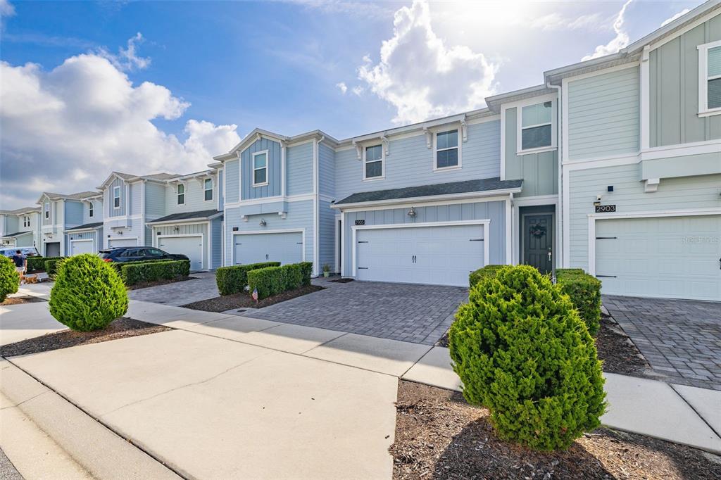 A row of light blue townhouses with paved driveways and green shrubs in the foreground — 2905 SATIRE STREET, KISSIMMEE, FL
