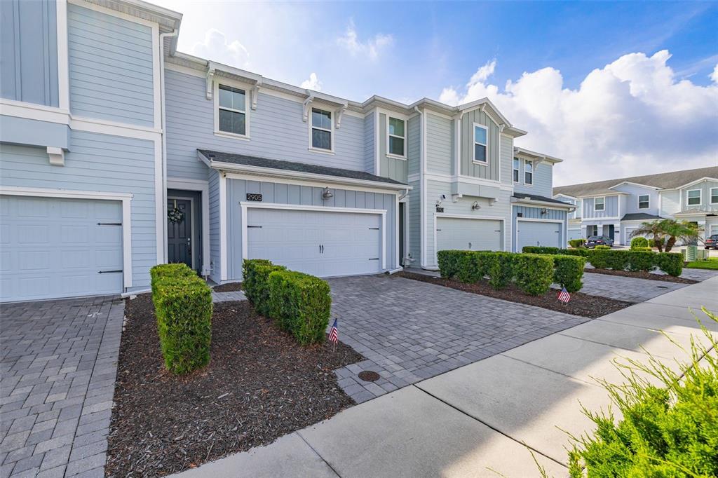 A row of light blue townhouses with attached garages and paved driveways under a blue sky — 2905 SATIRE STREET, KISSIMMEE, FL