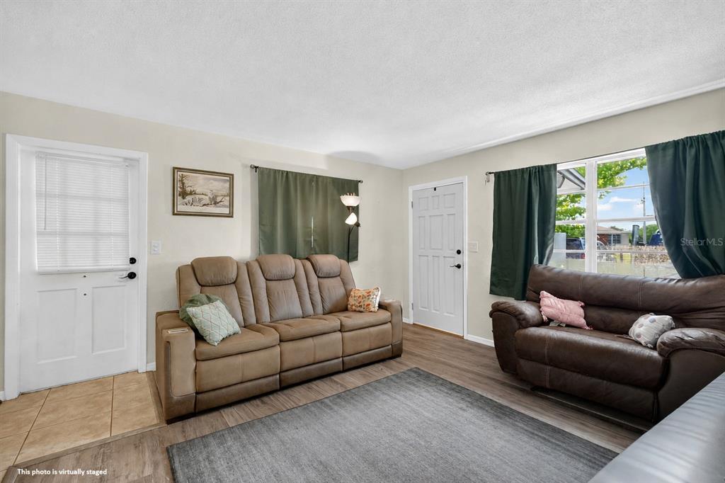 A living room features two brown sofas, wood-look flooring, and two white exterior doors — 1500 PRIMROSE LANE, DAYTONA BEACH, FL