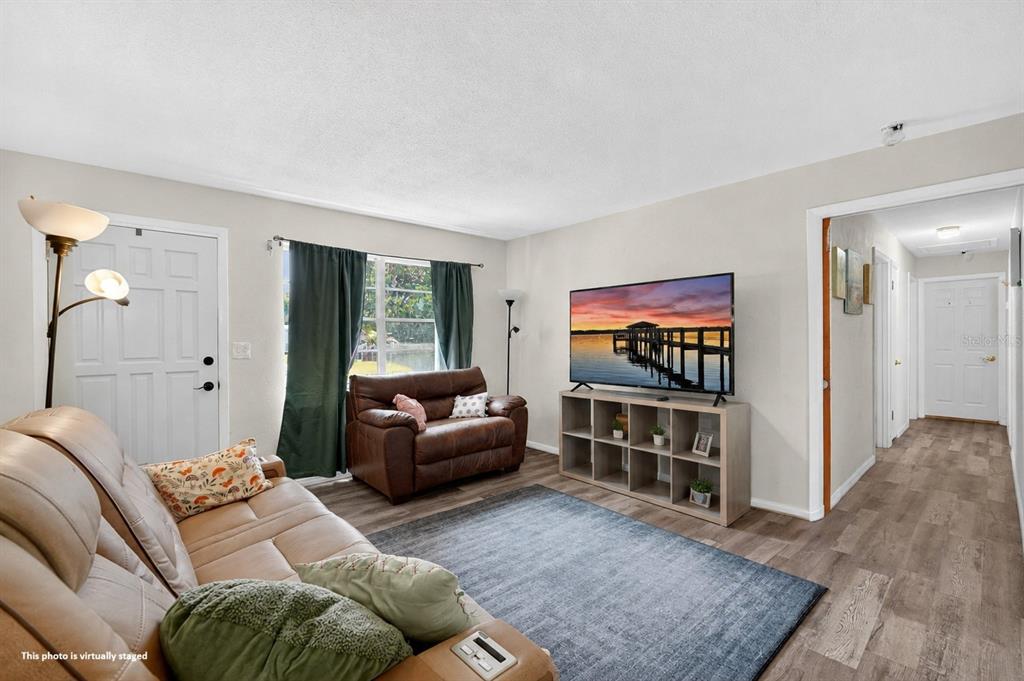 A living room features a tan sofa, a brown armchair, a television, and wood-look flooring — 1500 PRIMROSE LANE, DAYTONA BEACH, FL