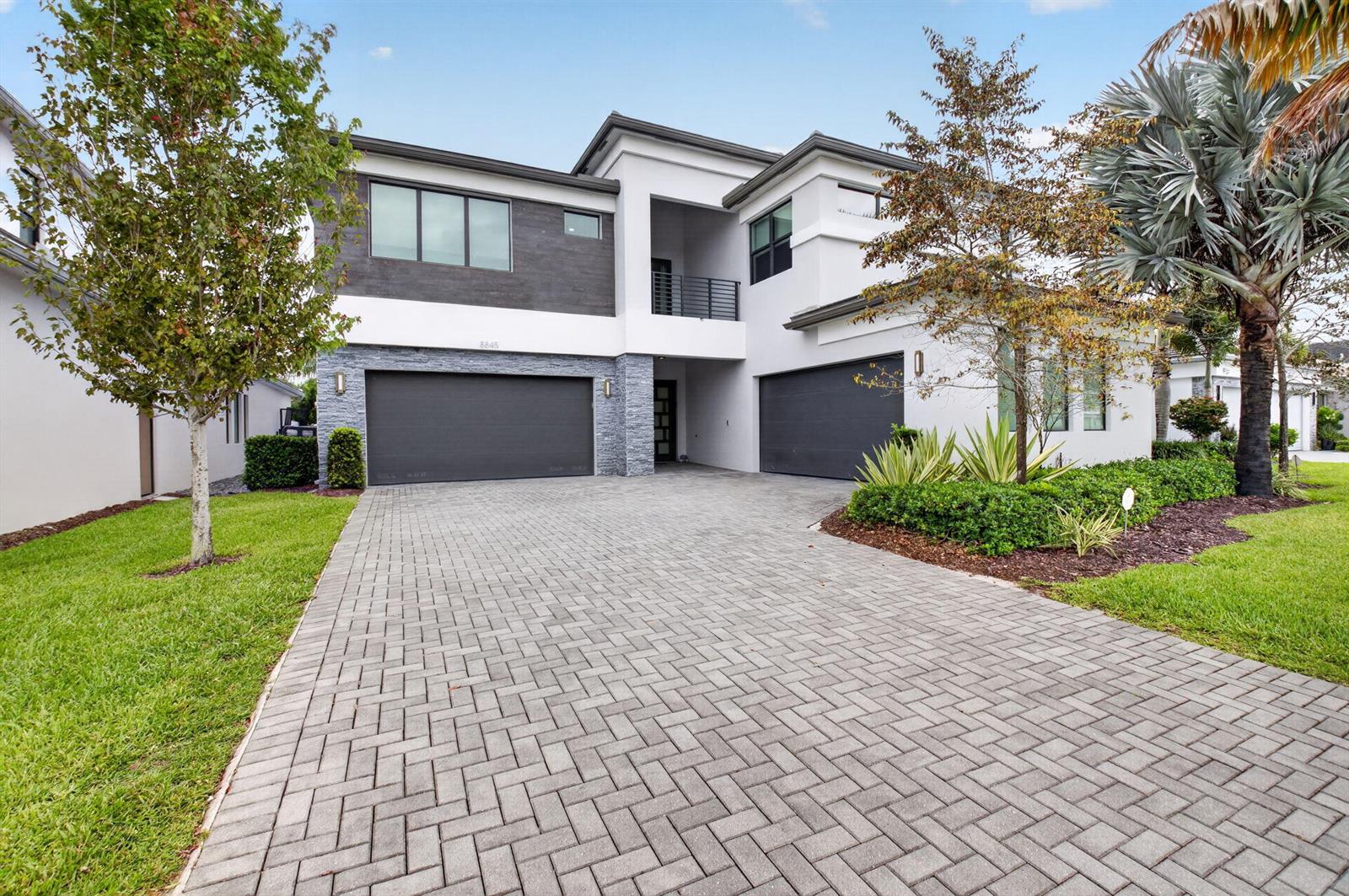 A two-story modern house features a paved driveway, two garage doors, and stone accents — 8845 Skyward Street, Boca Raton FL 33496, BOCA RATON, FL