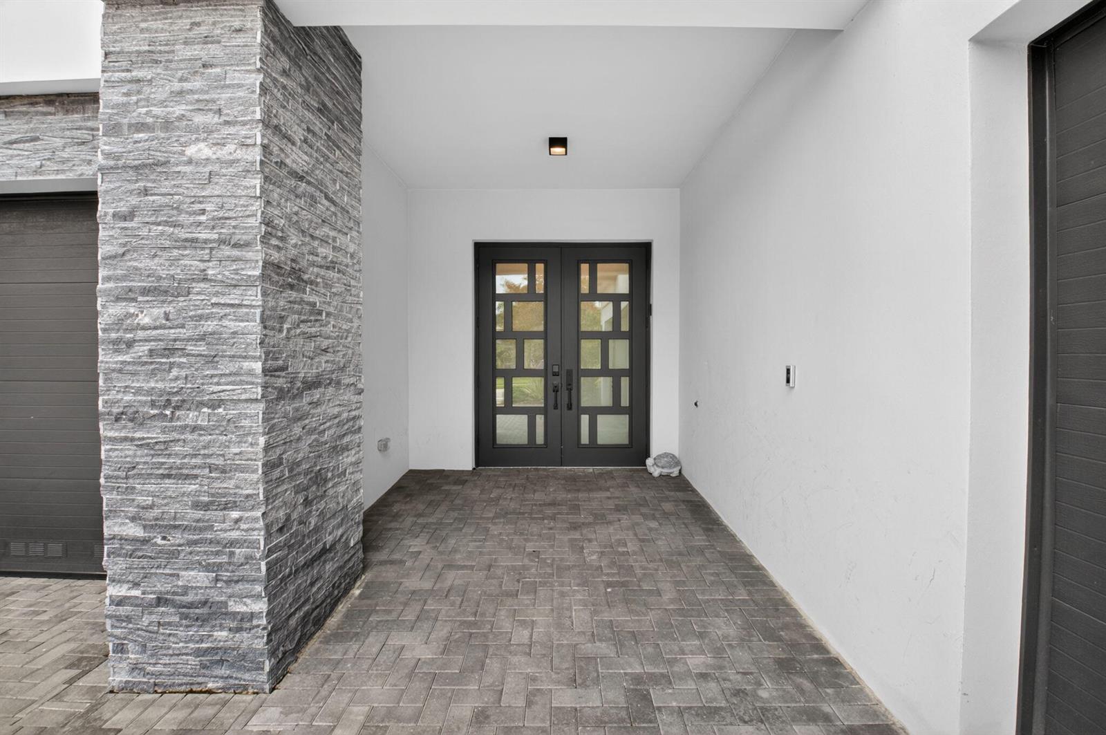 A covered entryway features a stone pillar, paver flooring, and double glass-paneled front doors — 8845 Skyward Street, Boca Raton FL 33496, BOCA RATON, FL