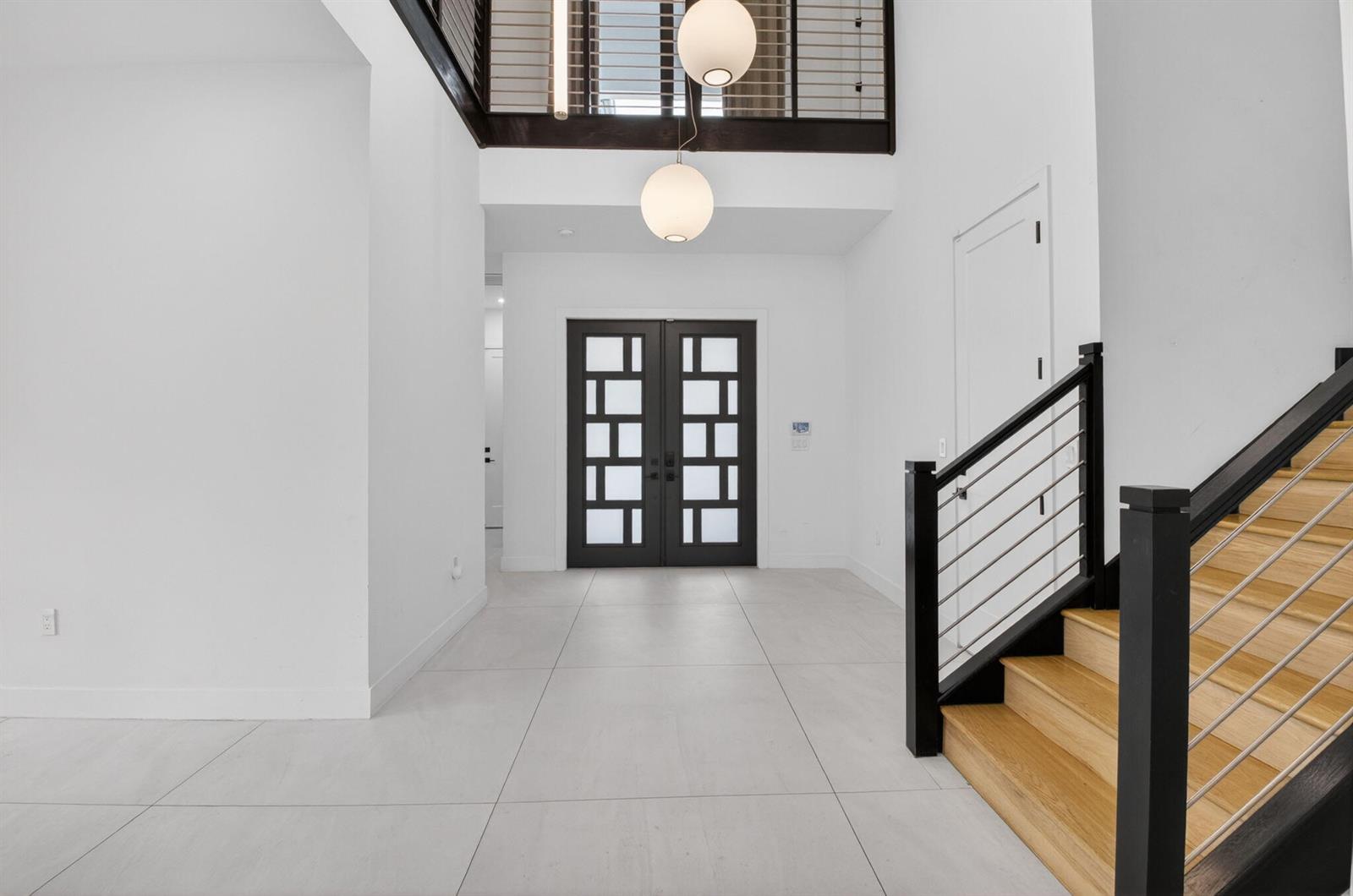 A modern entryway features white tile floors, a double front door, and a wooden staircase — 8845 Skyward Street, Boca Raton FL 33496, BOCA RATON, FL