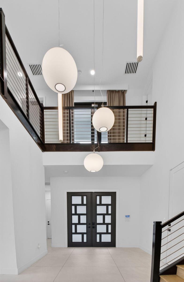 A modern entryway features a double-height ceiling, pendant lights, and a dark wood balcony railing — 8845 Skyward Street, Boca Raton FL 33496, BOCA RATON, FL