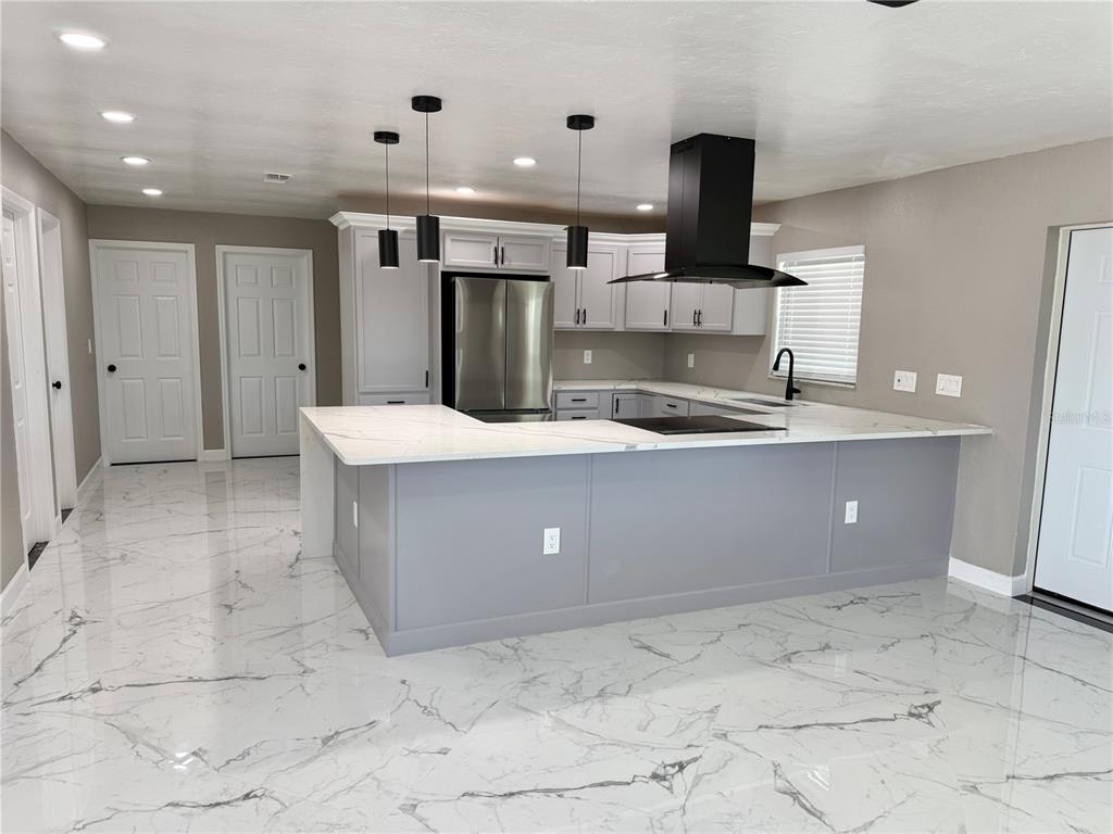 A modern kitchen features a large island with white marble countertops and gray cabinetry — 715 65TH AVENUE DRIVE W, BRADENTON, FL