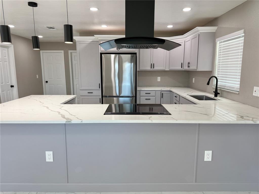 A kitchen features light gray cabinets, white marble-look countertops, a black range hood, and stainless-steel appliances — 715 65TH AVENUE DRIVE W, BRADENTON, FL