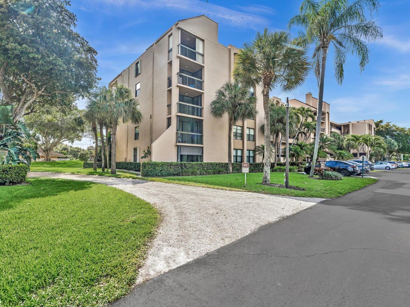 A multi-story beige apartment building stands next to a paved road and palm trees — 2455 Lindell Boulevard # 3401, Delray Beach FL 33444, DELRAY BEACH, FL