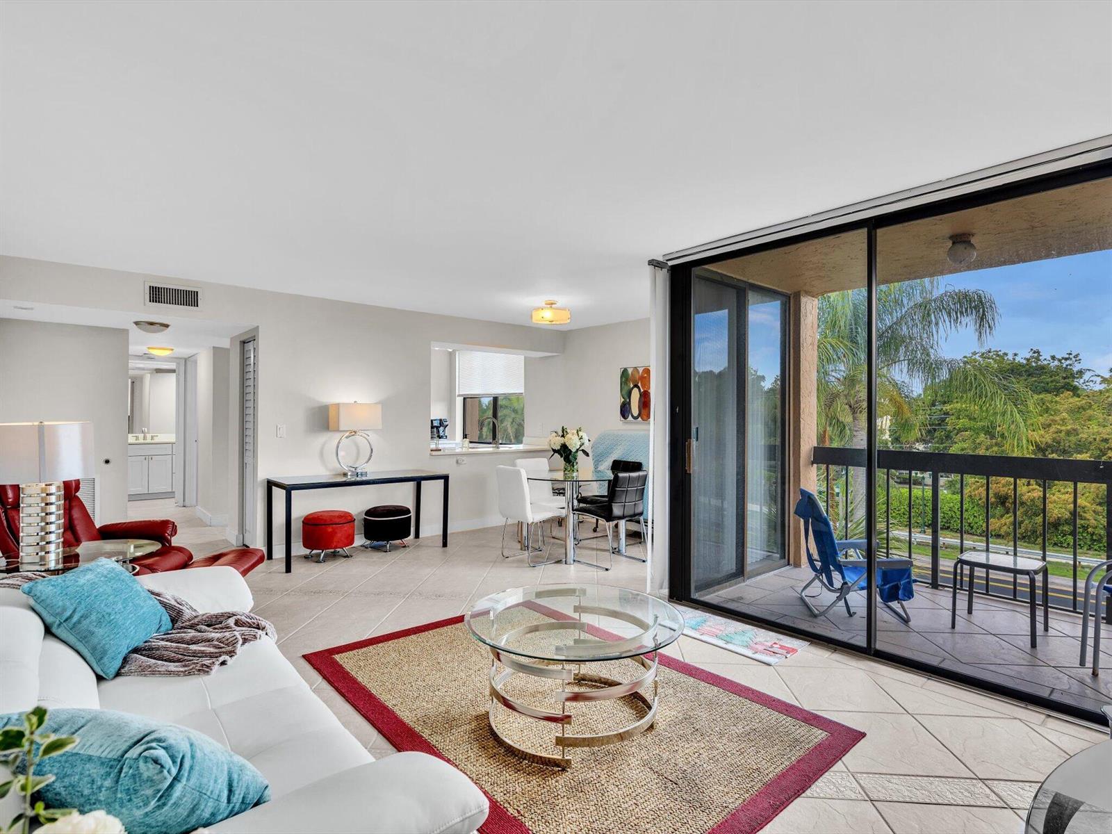A living room with tile floors, a glass coffee table, and a balcony with palm trees — 2455 Lindell Boulevard # 3401, Delray Beach FL 33444, DELRAY BEACH, FL