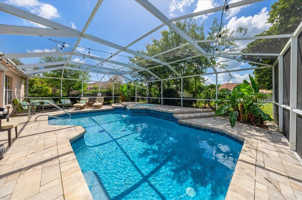 A screened-in patio features a swimming pool with a spillover spa and paver decking — 1302 LOPEZ LANE, THE VILLAGES, FL