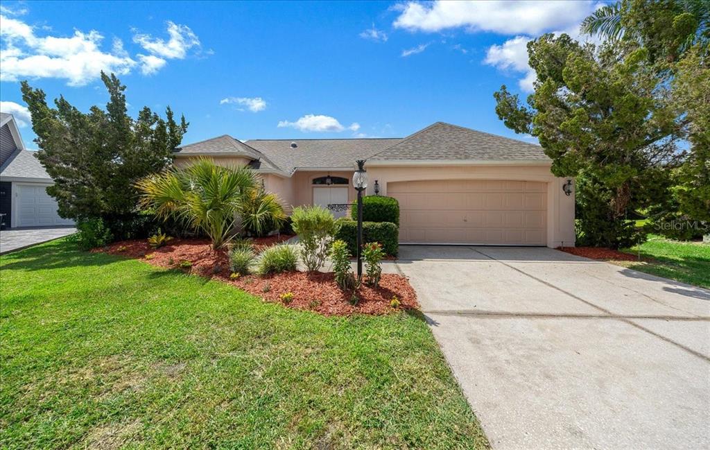 A concrete walkway leads to the double front doors of a light-colored stucco house — 1302 LOPEZ LANE, THE VILLAGES, FL