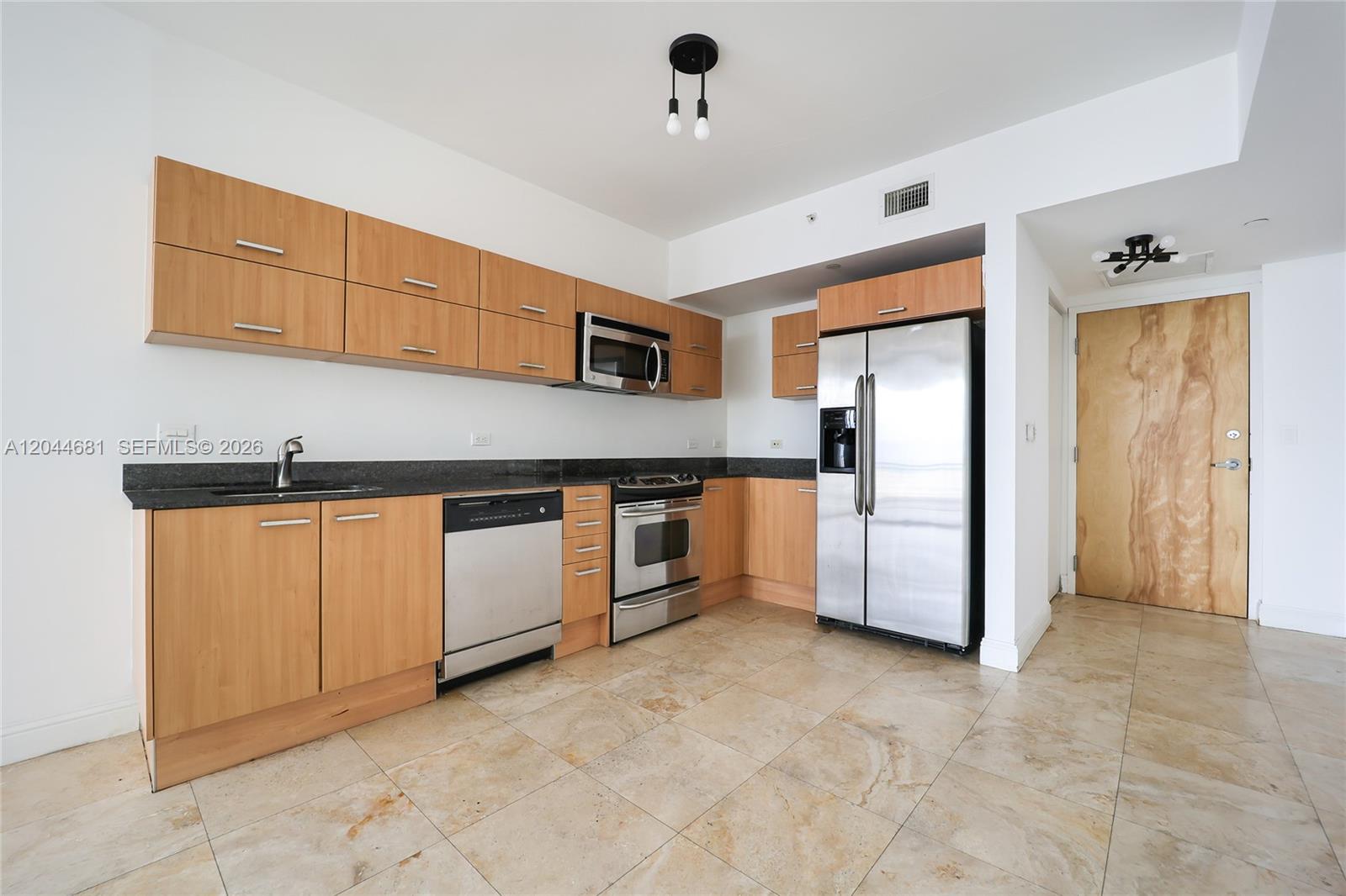 A kitchen features light wood cabinets, stainless steel appliances, dark countertops, and beige tile flooring — 350 S Miami Ave # 2411, Miami FL 33130, MIAMI, FL