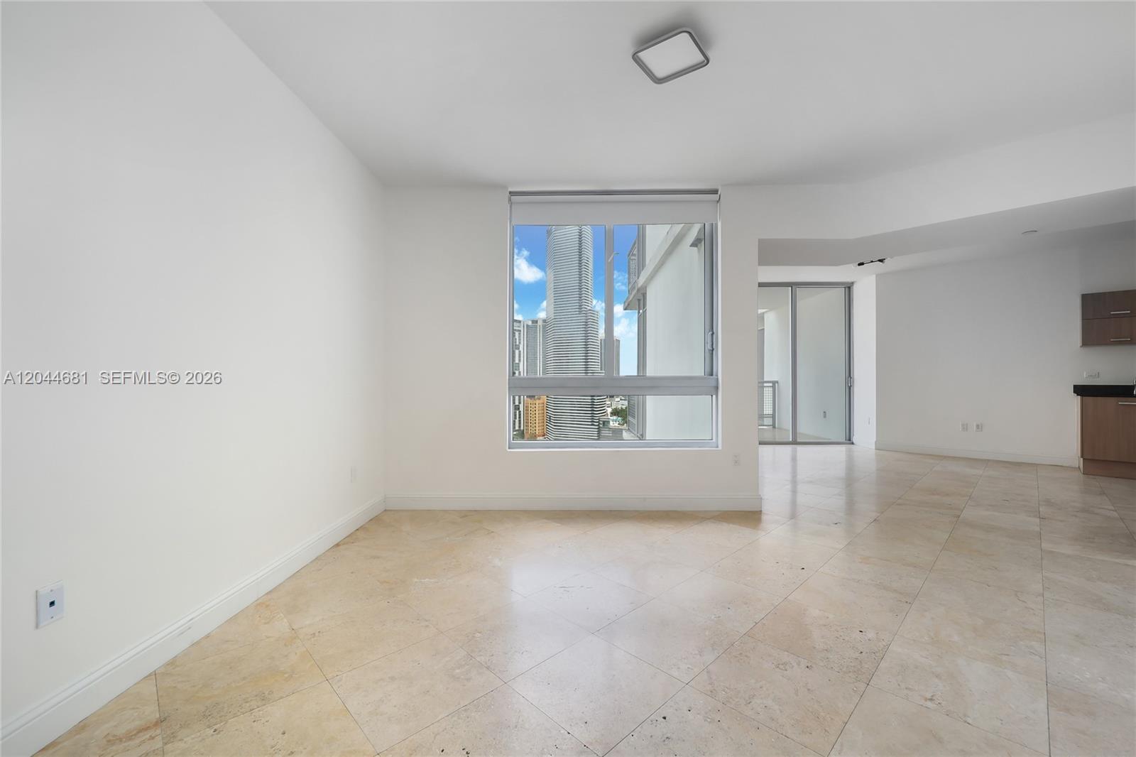An empty room with beige tile flooring, white walls, a central window, and a kitchen area — 350 S Miami Ave # 2411, Miami FL 33130, MIAMI, FL
