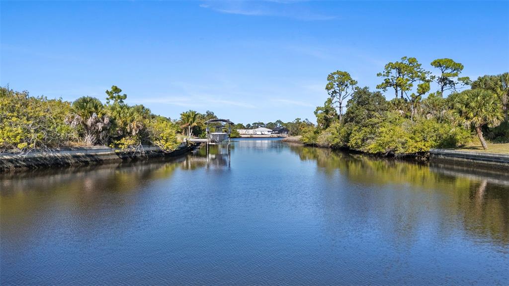 A canal flows between lush green trees toward a boat lift and distant houses — 1387 GLANMORE DRIVE, PORT CHARLOTTE, FL