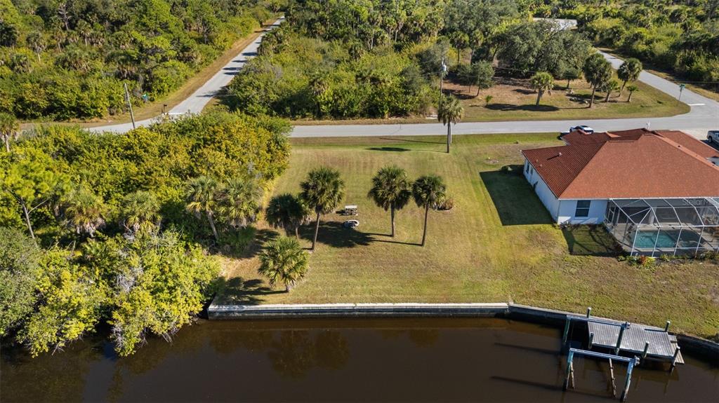 An aerial view shows a waterfront lot with a seawall, dock, and palm trees — 1387 GLANMORE DRIVE, PORT CHARLOTTE, FL