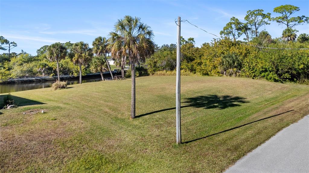 A grassy, vacant lot features several palm trees and a utility pole near a canal — 1387 GLANMORE DRIVE, PORT CHARLOTTE, FL