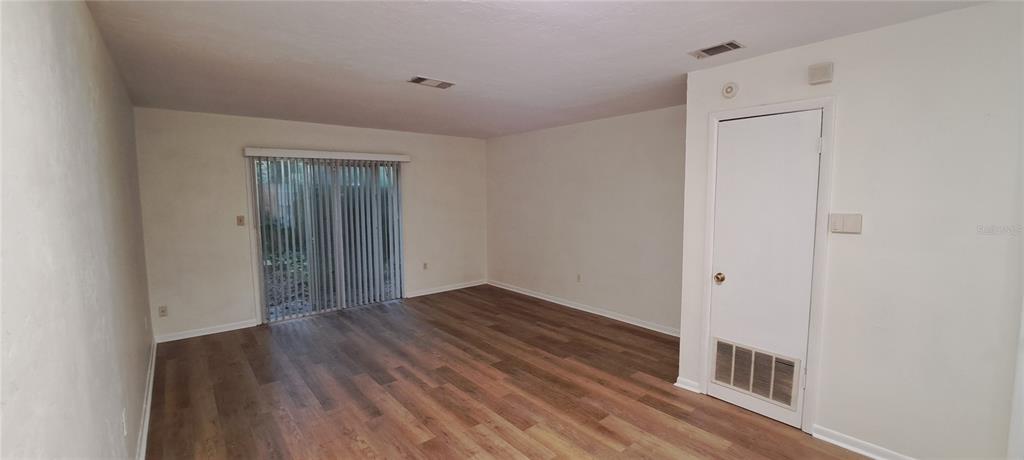 An empty room features wood-look flooring, white walls, and a sliding glass door — 3925 SW 26TH TERRACE UNIT B, GAINESVILLE, FL