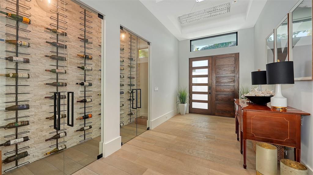 A modern entryway features a glass-enclosed wine cellar, wood front door, and light hardwood floors — 1421 N LAKE SHORE DRIVE, SARASOTA, FL