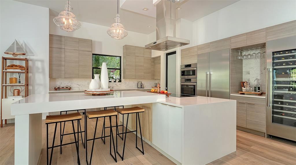 A modern kitchen features light wood cabinetry, a white waterfall island, and stainless steel appliances — 1421 N LAKE SHORE DRIVE, SARASOTA, FL