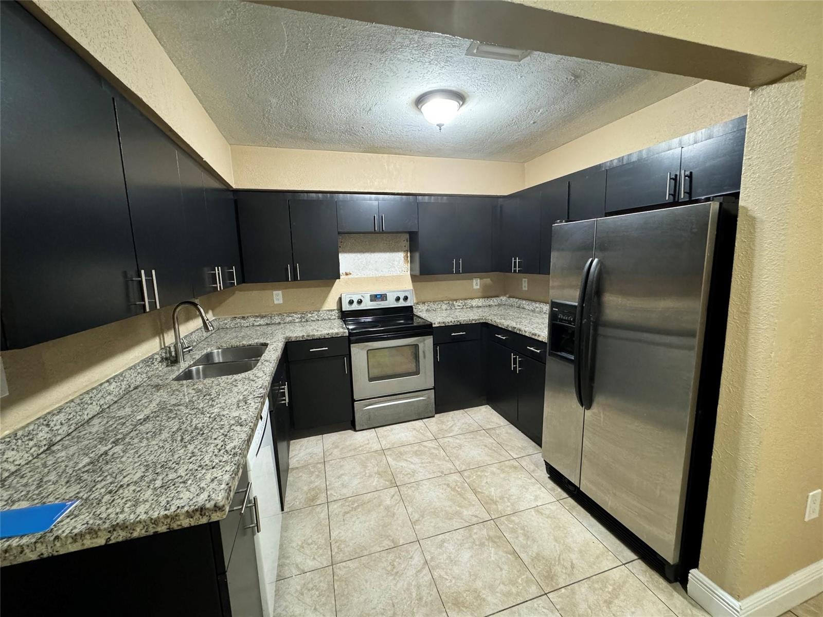 A kitchen features dark cabinets, granite countertops, stainless steel appliances, and light tile flooring — 2091 Oleander Drive, Miramar FL 33023, MIRAMAR, FL
