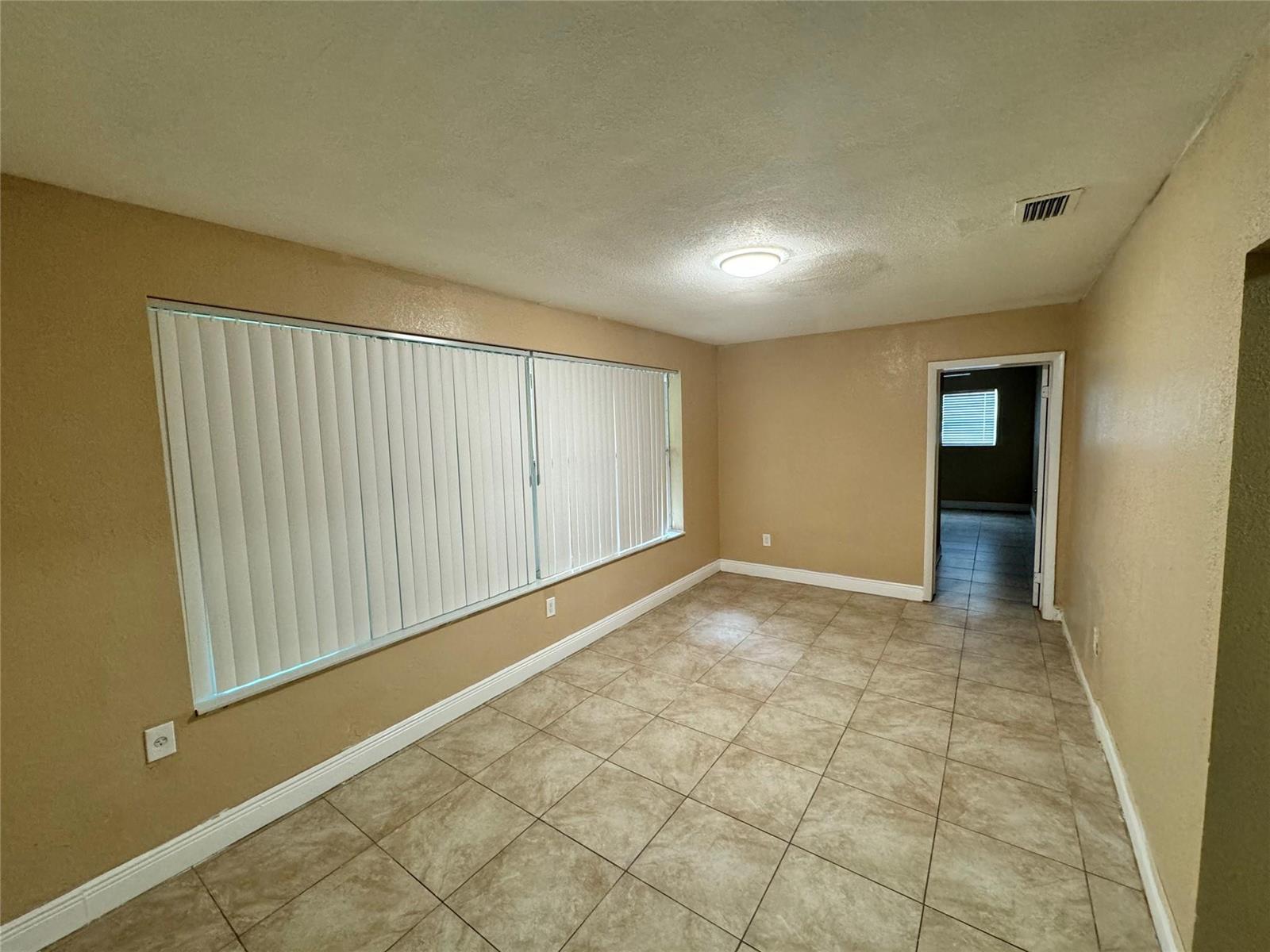 An empty room features tan walls, tile flooring, vertical blinds, and a doorway to another room — 2091 Oleander Drive, Miramar FL 33023, MIRAMAR, FL
