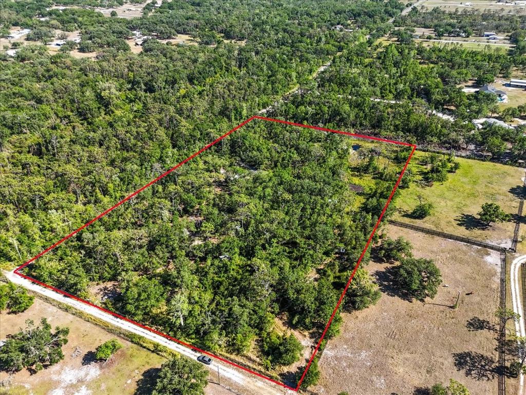 An aerial view shows a rectangular, wooded lot outlined in red next to a dirt road — 24820 49TH AVENUE E, MYAKKA CITY, FL